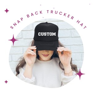 Może przedstawiać: Czarna czapka typu trucker z zatrzaskiem z napisem "CUSTOM" białymi literami. Czapka jest noszona przez osobę. Słowa "SNAP BACK TRUCKER HAT" są napisane p&oacute;łkolem nad czapką.