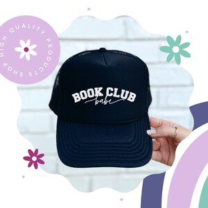 Peut inclure: Casquette de camionneur noire en mesh avec un texte brod&eacute; blanc qui dit "BOOK CLUB babe".