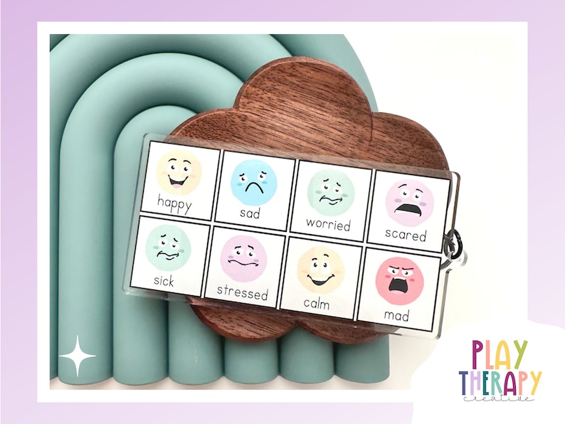 May include: A set of emotion flashcards with illustrations of faces expressing different feelings, including happy, sad, and mad. The cards are displayed on a wooden cloud-shaped holder, with a light blue arch in the background.