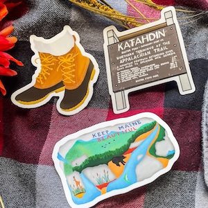 May include: Two stickers featuring a pair of brown hiking boots and a map of Maine. The map sticker has the text "Keep Maine Beautiful" and features a bear, a deer, and a river. The sign sticker has the text "Katahdin Baxter Peak - Elevation 5267 ft. Northern Terminus of the Appalachian Trail A Mountain Footpath Extending Over 2000 Miles to Springer Mtn. Georgia."