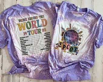 May include: Two purple tie-dye t-shirts with a bleach-splattered effect. One shirt features the text "Drink Around the World 19 Tour 82" with a list of cities. The other shirt features a graphic of the Epcot logo and Mickey Mouse characters.