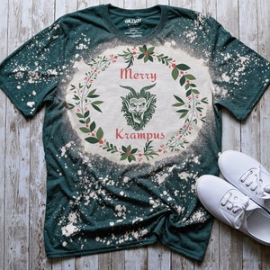 May include: A green t-shirt with a bleach-splattered design featuring a wreath with the text "Merry Krampus" and a cartoon Krampus inside the wreath.