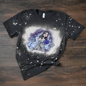 May include: A black t-shirt with a bleach-splattered design featuring a cartoon bride with a bouquet of flowers. The bride has a pale complexion, dark hair, and a white dress.