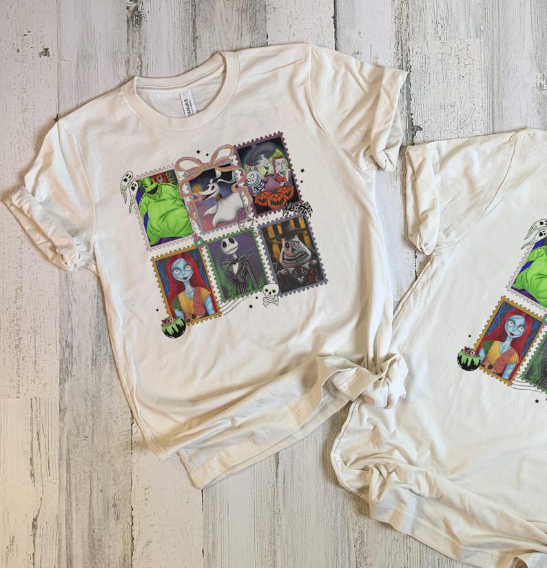 May include: Two white t-shirts with a colourful graphic featuring characters from The Nightmare Before Christmas. The design is arranged in a stamp-like format, showcasing Jack Skellington, Sally, and other characters. The shirts are made of a soft material.
