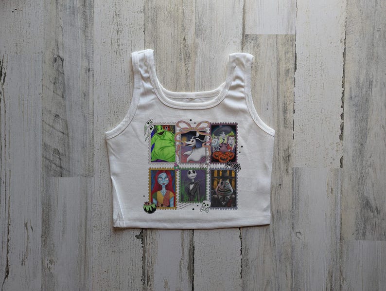 May include: White vest top with a colourful graphic of postage stamp-style images of characters from The Nightmare Before Christmas. The images include Jack Skellington, Sally, and Oogie Boogie. The vest top has a scoop neck and wide straps.