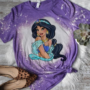 May include: Purple t-shirt with a bleach splattered design featuring a cartoon image of Princess Jasmine from Disney's Aladdin.
