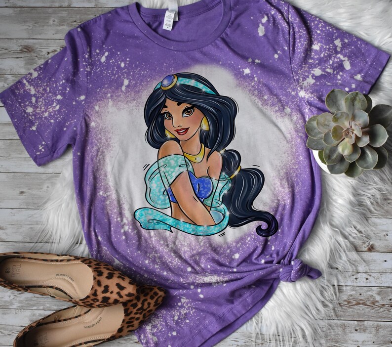 May include: Purple t-shirt with a bleach splattered design featuring a cartoon image of Princess Jasmine from Disney's Aladdin.