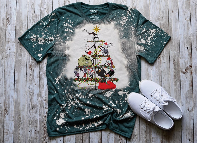 May include: A green t-shirt with a bleach-splattered design featuring a Christmas tree with characters from The Nightmare Before Christmas. The tree is decorated with ornaments and lights, and the characters are all wearing Santa hats.