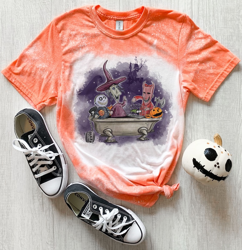 K&ouml;nnte beinhalten: Orangefarbenes Batik-T-Shirt mit einem Bleichmittel-Spritzeffekt. Das Shirt zeigt eine Grafik von Figuren aus dem Film Nightmare Before Christmas in einer Badewanne. Zu den Figuren geh&ouml;ren Jack Skellington, Sally und Oogie Boogie.