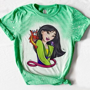 May include: Green t-shirt with a bleach-splattered design featuring a cartoon image of Mulan from Disney's Mulan, with Mushu the dragon and Cri-Kee the cricket.