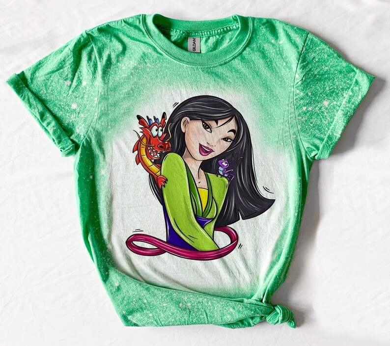 May include: Green t-shirt with a bleach-splattered design featuring a cartoon image of Mulan from Disney's Mulan, with Mushu the dragon and Cri-Kee the cricket.