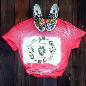 May include: Red t-shirt with a white bleach design of a green Krampus monster in a wreath with the text "Merry Krampus".