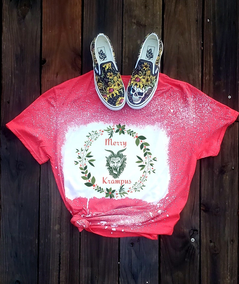 May include: Red t-shirt with a white bleach design of a green Krampus monster in a wreath with the text "Merry Krampus".