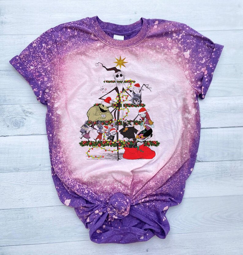 May include: A purple and white tie-dye t-shirt with a bleach-splattered design. The shirt features a graphic of characters from the Nightmare Before Christmas movie, arranged in a Christmas tree shape.