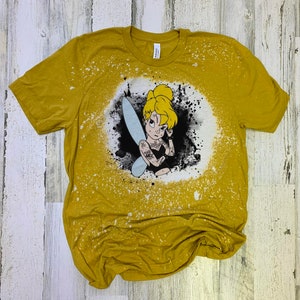 May include: A yellow t-shirt with a bleach-splattered design featuring a cartoon image of Tinkerbell with tattoos. The design is in black and white with a blue fairy wing.