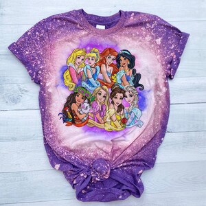May include: Purple tie-dye t-shirt with a bleach-splattered design featuring a group of Disney princesses, including Ariel, Belle, Cinderella, Moana, Rapunzel, Snow White, and Tiana.