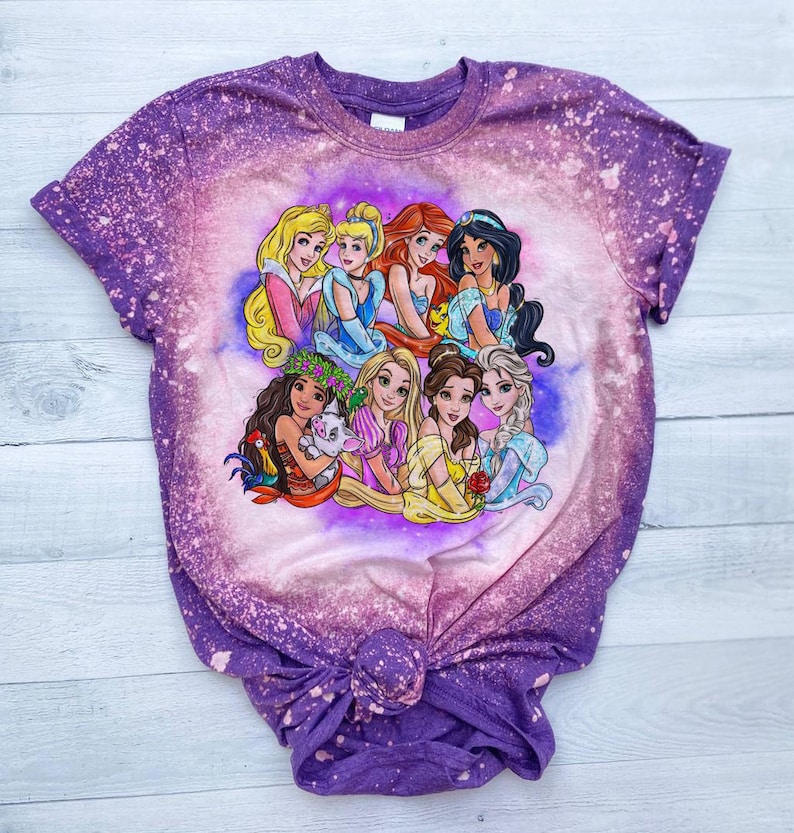 May include: Purple tie-dye t-shirt with a bleach-splattered design featuring a group of Disney princesses, including Ariel, Belle, Cinderella, Moana, Rapunzel, Snow White, and Tiana.