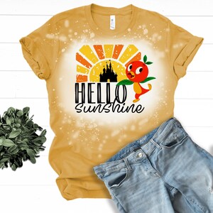 May include: A yellow t-shirt with a bleach-splattered design featuring a cartoon bird, a castle silhouette, and the text "Hello Sunshine".