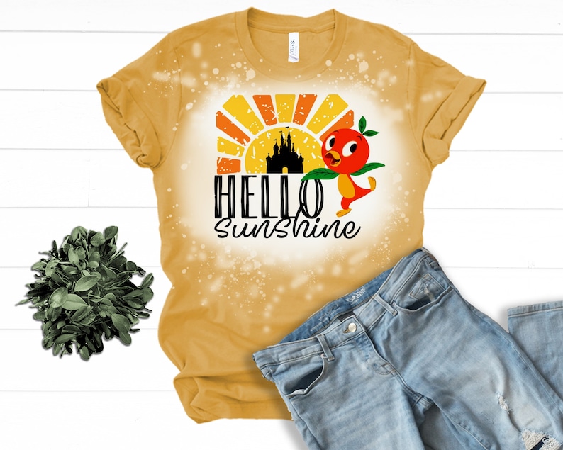 May include: A yellow t-shirt with a bleach-splattered design featuring a cartoon bird, a castle silhouette, and the text "Hello Sunshine".
