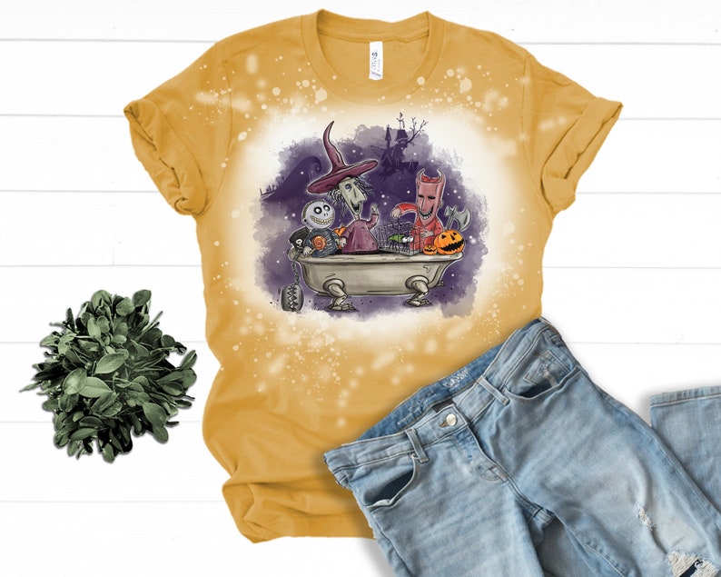 K&ouml;nnte beinhalten: Ein gelbes T-Shirt mit einem Design aus Bleichmittelspritzern, das ein Cartoon-Bild von Figuren aus dem Film Nightmare Before Christmas zeigt. Die Figuren befinden sich in einer Badewanne mit K&uuml;rbissen und anderen Halloween-Dekorationen.