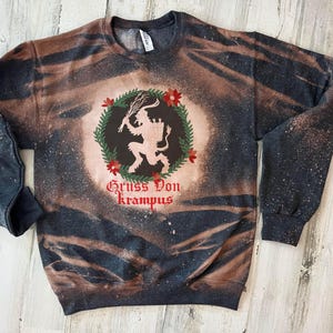 May include: Black and brown tie-dye sweatshirt with a white silhouette of a Krampus figure inside a wreath with red berries and the text "Gruss Von Krampus".