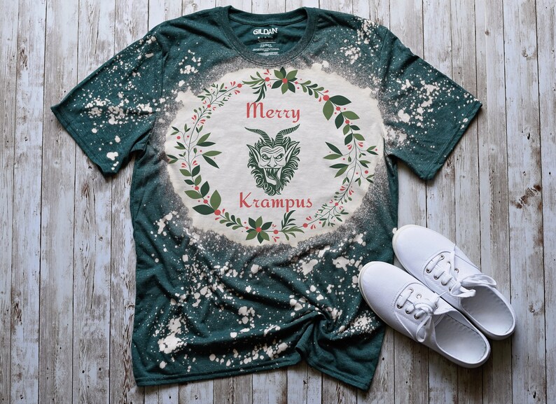 May include: A green t-shirt with a bleach-splattered design featuring a wreath with the text "Merry Krampus" and a cartoon Krampus inside the wreath.