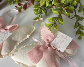 May include: Two butterfly-shaped fabric ornaments in off-white with pink ribbon bows. Each ornament features a small square tag with pink decorative borders and the text 'Hoş Geldin Gökçe' attached by a thin pink ribbon loop for hanging.