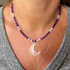 May include: A purple and white beaded necklace with a crescent moon pendant made of clear quartz.
