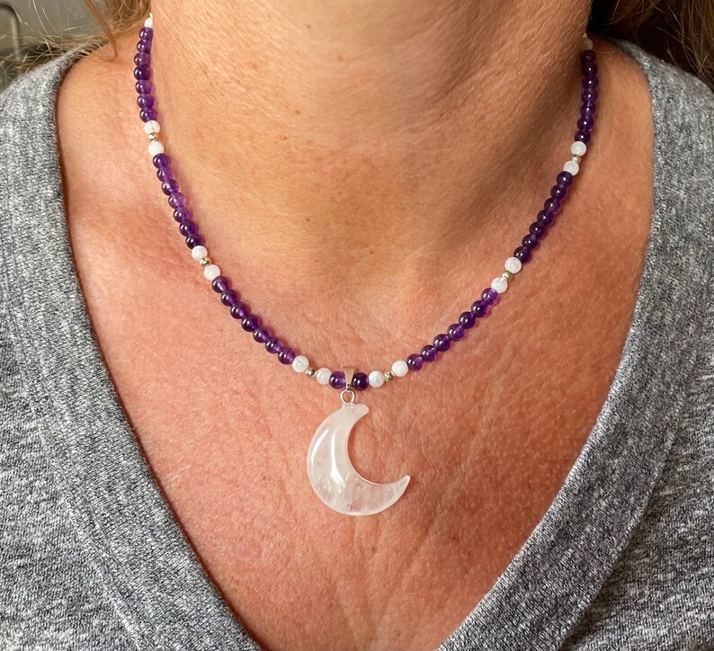 May include: A purple and white beaded necklace with a crescent moon pendant made of clear quartz.
