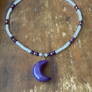 May include: A white and purple beaded necklace with a purple crescent moon pendant.