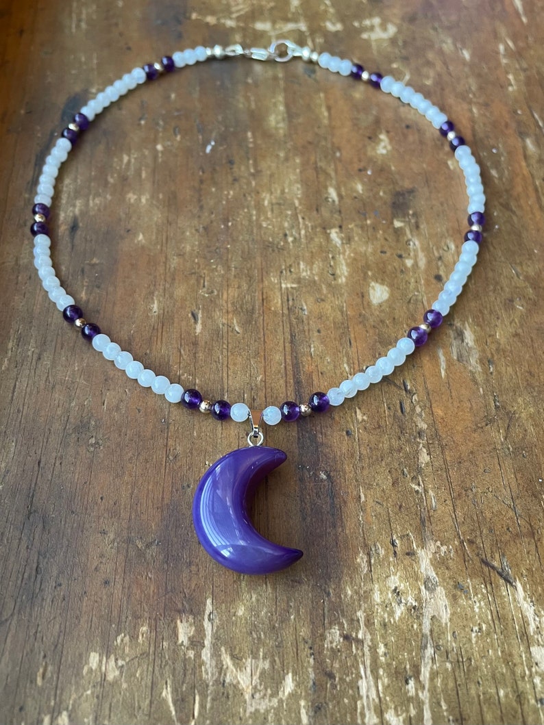 May include: A white and purple beaded necklace with a purple crescent moon pendant.