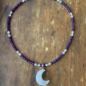 May include: A necklace made with amethyst and moonstone beads with a crescent moon pendant made of white quartz.