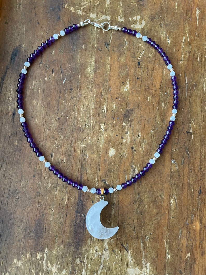 May include: A necklace made with amethyst and moonstone beads with a crescent moon pendant made of white quartz.