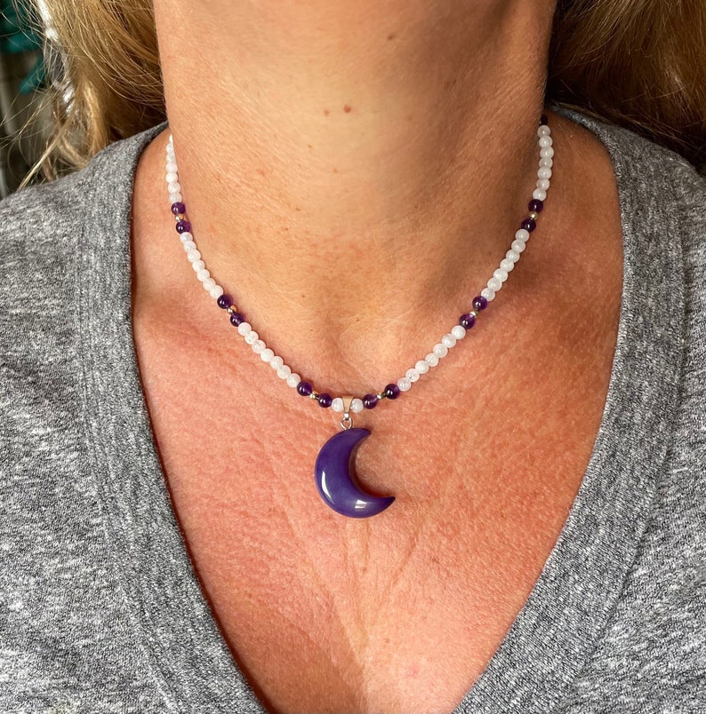 May include: A white and purple beaded necklace with a purple crescent moon pendant.