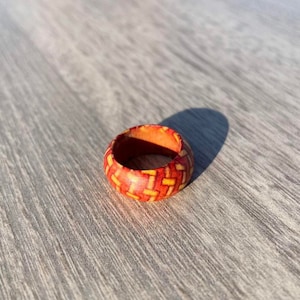 Puede incluir: Un anillo de madera con un patrón geométrico rojo y amarillo. El anillo está hecho de madera y tiene un acabado liso.