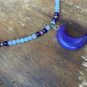 May include: A silver chain necklace with light blue and purple beads and a purple crescent moon pendant.