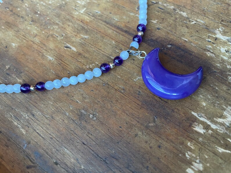May include: A silver chain necklace with light blue and purple beads and a purple crescent moon pendant.