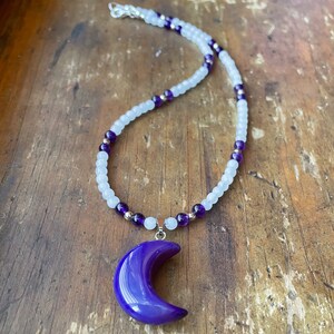 May include: A purple crescent moon pendant necklace with a white and purple beaded chain.