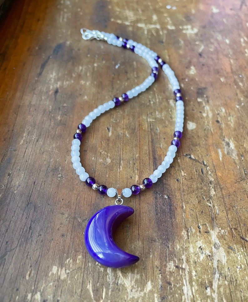 May include: A purple crescent moon pendant necklace with a white and purple beaded chain.