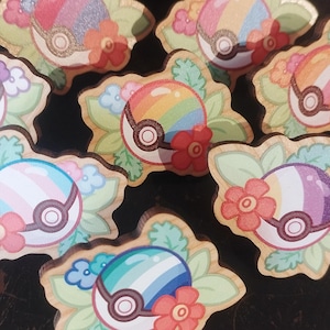 Peut inclure: Une collection d'épingles en bois avec des motifs colorés. Chaque épingle présente une balle stylisée avec des accents floraux et une bordure en forme de feuille. Les balles affichent des couleurs arc-en-ciel, pastel et autres couleurs vives.