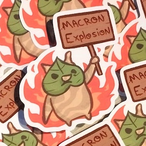Peut inclure: Une collection d'autocollants représentant un personnage de dessin animé tenant une pancarte sur laquelle est écrit "Macron Explosion". Le personnage est une créature à peau verte avec une feuille sur la tête, et il est entouré de flammes.