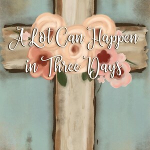 May include: A wooden cross with a light brown color, adorned with peach and pink flowers. The text "A Lot Can Happen in Three Days" is written across the cross in elegant script. The background is a soft, muted blue.