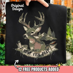 Op de afbeelding: Zwart sweatshirt met een camouflage hertenafbeelding, bergen en een vislokmiddel. De banner leest "HUNT. FISH. PRAY.". De tekst "Original Design" staat linksboven. De onderkant heeft de tekst "12 FREE PRODUCTS ADDED".