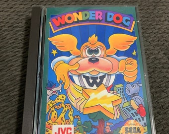 May include: A Sega CD game case featuring a colourful illustration of a cartoon dog with wings, a star, and the text "Wonder Dog". The case also includes the Sega logo and the text "Licensed by Sega of America, Inc. for play on the Sega CD".