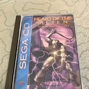 May include: A Sega CD game case for "Heart of the Alien: Out of This World Parts I and II". The cover art features a muscular, humanoid alien wielding a whip in a dark, stormy setting. The game is rated MA-13 for Mature Audiences.
