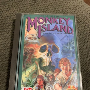 Puede incluir: Una caja de juego Sega CD para The Secret of Monkey Island de LucasArts. La caja presenta una ilustración colorida de una calavera, un mono y un pirata.
