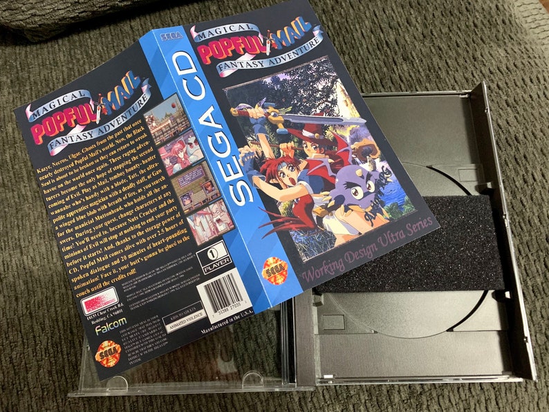 May include: A Sega CD game case for "Magical Pop'n Mail: Fantasy Adventure" is open, revealing the game's CD and packaging. The box art features colorful anime-style characters. The case is silver with a black foam insert.