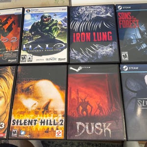 May include: Eight video game cases arranged in two rows. Top row: Halo 2, Halo Combat Evolved, Iron Lung, and Sons of the Forest. Bottom row: Silent Hill 3, Silent Hill 2, Dusk, and Slender. Each case features distinct cover art and titles.