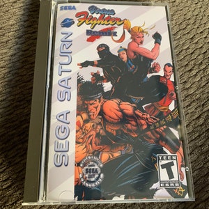 Puede incluir: Una caja de juego de Sega Saturn con un fondo blanco y una imagen colorida de personajes del juego "Virtua Fighter Remix". El juego está clasificado como "Teen" por la ESRB.