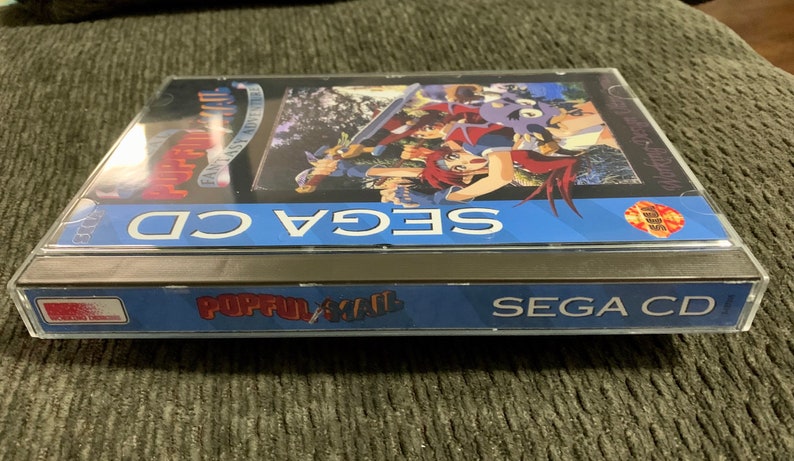 May include: A SEGA CD game case for Popful Mail: Fantasy Adventure. The case is clear with a blue band that reads "SEGA CD" and "Popful Mail". The game cover art features anime-style characters with swords.
